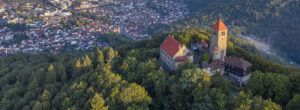 Drohnenbild der Wachenburg in Weinheim. Die Burg ist von der Sonne angestrahlt und umgeben von Wald. Im Hintergrund Blick auf Weinheim