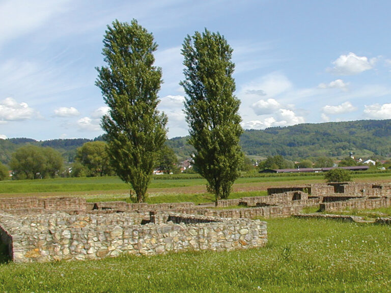 Mauerreste der ehemaligen Villa Rustica, dahinter Bäume, außenrum Feld. Im Hintergrund die Hügelkette der Bergstraße