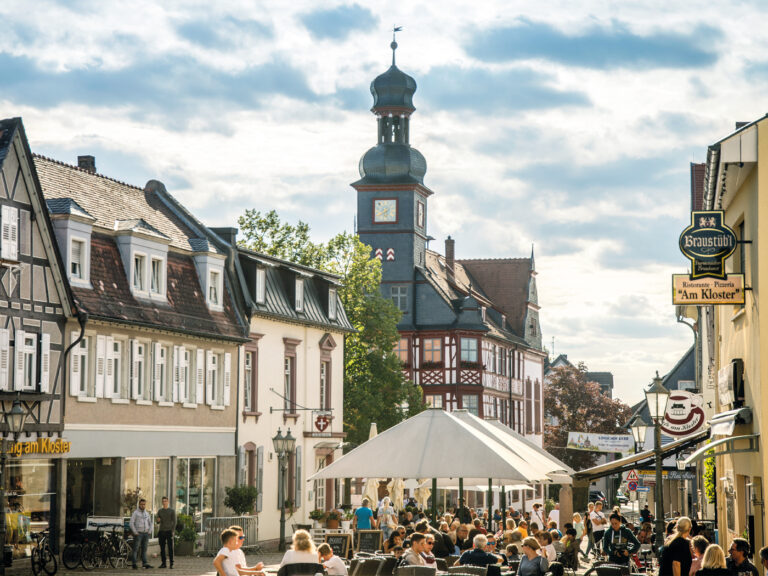 Platz am Kloster Lorsch mit Blick auf das Rathaus. Menschen sitzen auf den Restaurant-Terrassen bei sonnigem Wetter.