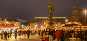 Gemütliche Abendstimmung auf dem Weihnachtsmarkt in Darmstadt. Menschen stehen zusammen und unterhalten sich. Blick auf die Reiterstatue von Großherzog Ludwig IV und das Hessische Landesmuseum auf dem Paradeplatz