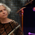 Das Bild ist zweigeteilt. Im rechten Teil sieht man einen Schlagzeugspieler in atmosphärischem Licht. Im linken Teil sieht man eine Frau die gedankenverloren in die Ferne blickt und eine Querflöte in der Hand hält