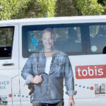 Ein Kleinbus mit flächiger Werbung zur Sendung Tobias Städtetrip steht in den Weinbergen