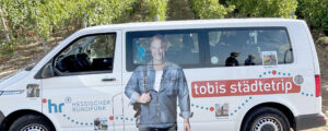 Ein Kleinbus mit flächiger Werbung zur Sendung Tobias Städtetrip steht in den Weinbergen
