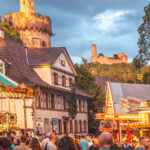 Abendstimmung in der Weinheimer Altstadt. Zahlreiche Menschen sind um Buden und bunte Karussell versammelt. Im Hintergrund der beleuchtete Rote Turm und die Burg Windeck