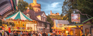 Abendstimmung in der Weinheimer Altstadt. Zahlreiche Menschen sind um Buden und bunte Karussell versammelt. Im Hintergrund der beleuchtete Rote Turm und die Burg Windeck
